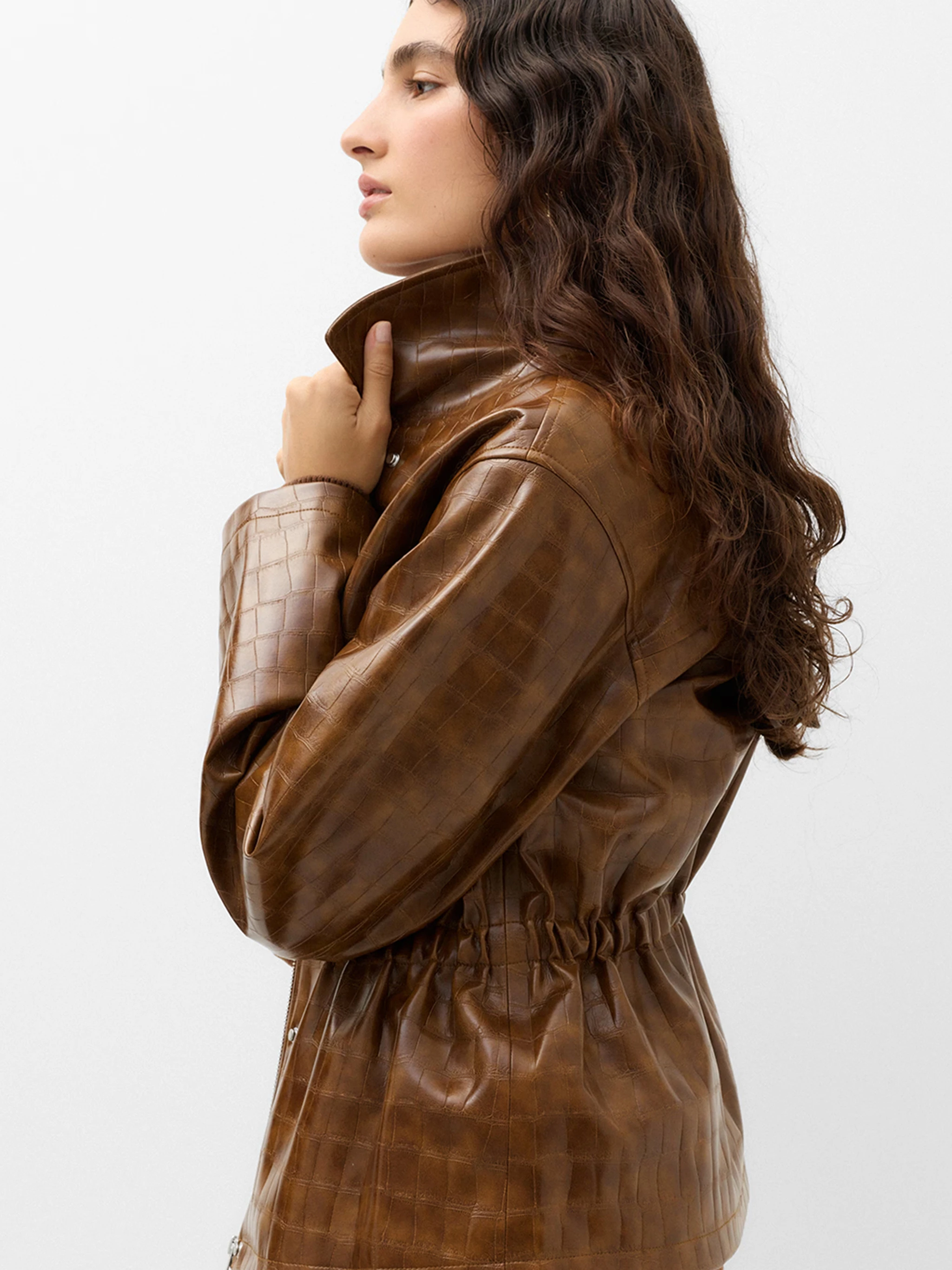 Women in a croc textured brown jacket with a cinched waist and high collar.