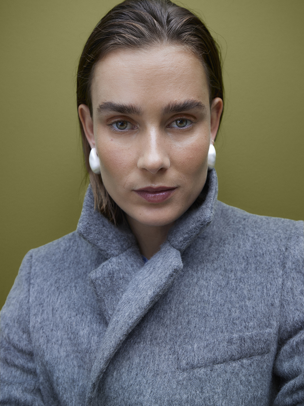 Woman wearing silver oversized earrings and a grey overcoat