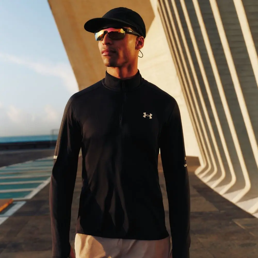 A man wears an Under Armour sports gear and a baseball cap and sunglasses