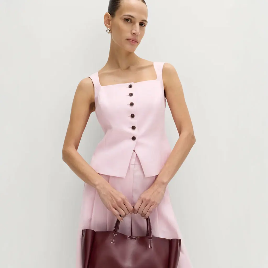 Woman wearing a pink waistcoat with matching trousers, silver jewellery and a burgundy bag