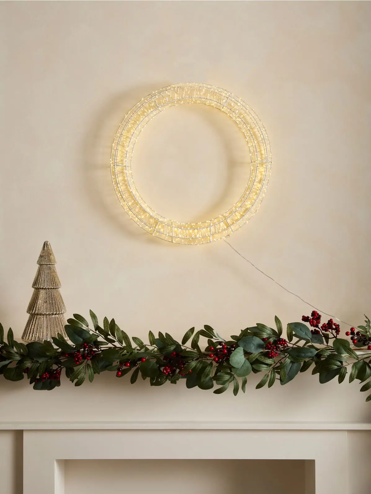 Lit up wreath wall decoration above mantelpiece adorned with green foliage