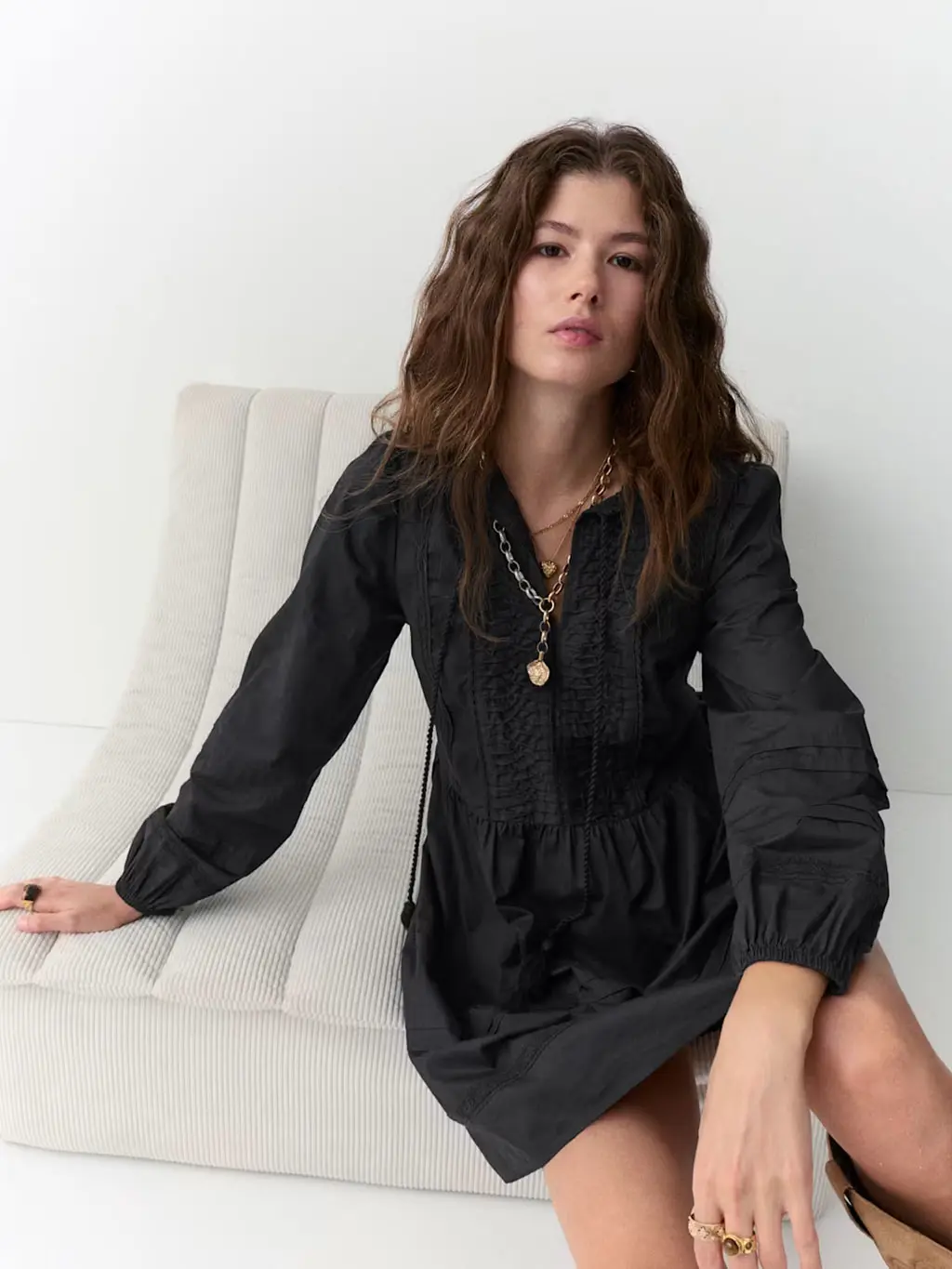 Woman wearing a black mini dress with layered gold jewellery and brown suede boots