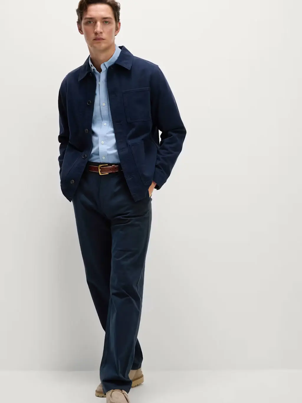 Man wearing navy chinos with a blue shirt, navy overshirt and brown suede shoes