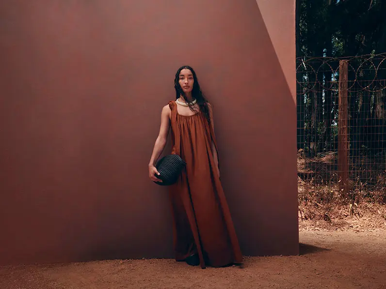 Woman wearing a rust-toned dress with a chunky beaded necklace and a black bag