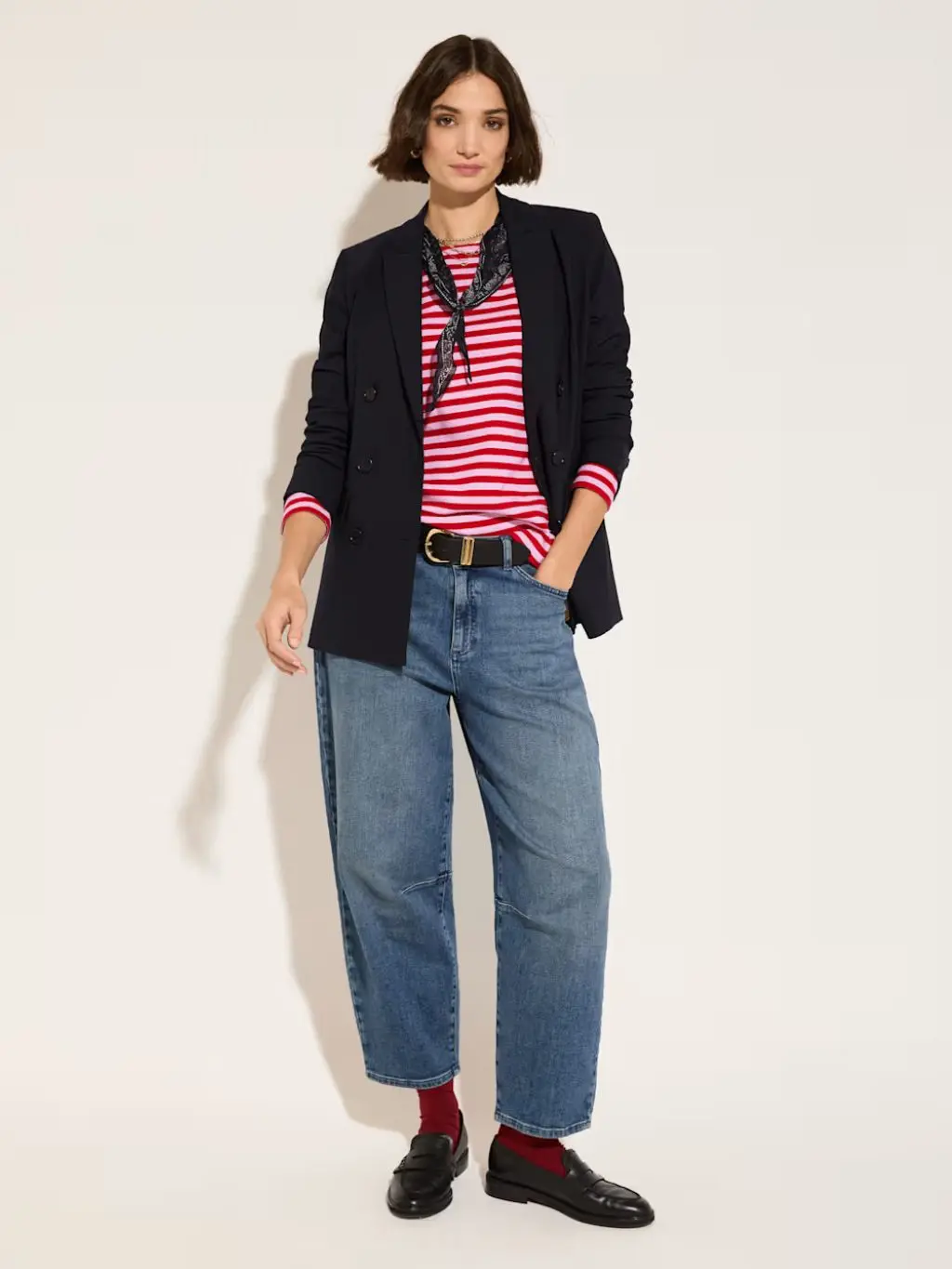 A woman wears a striped top, blazer, neck scarf, jeans and loafers with socks