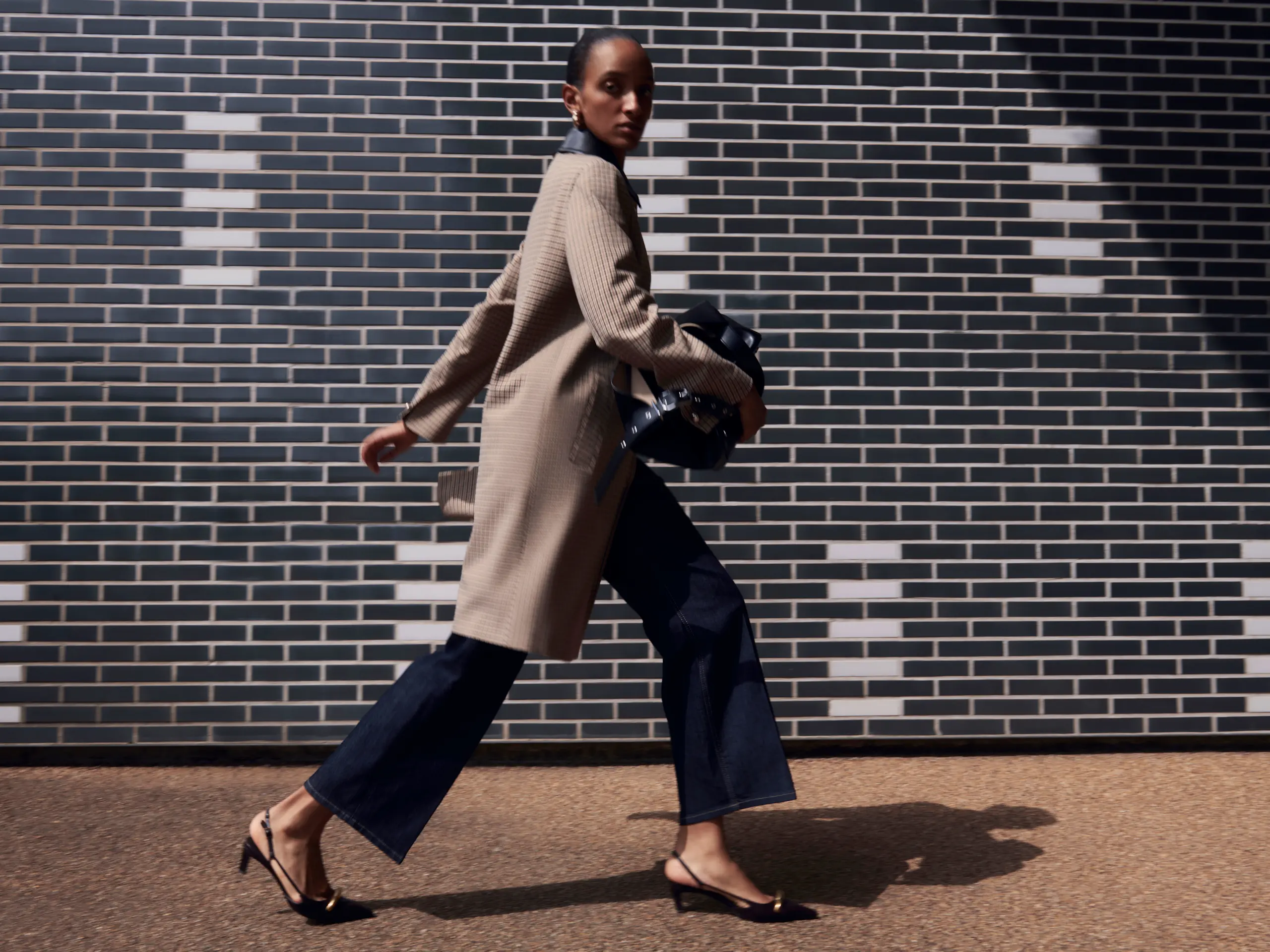 Woman wearing beige coat, dark blue denim, black kitten heels and holding a black bag