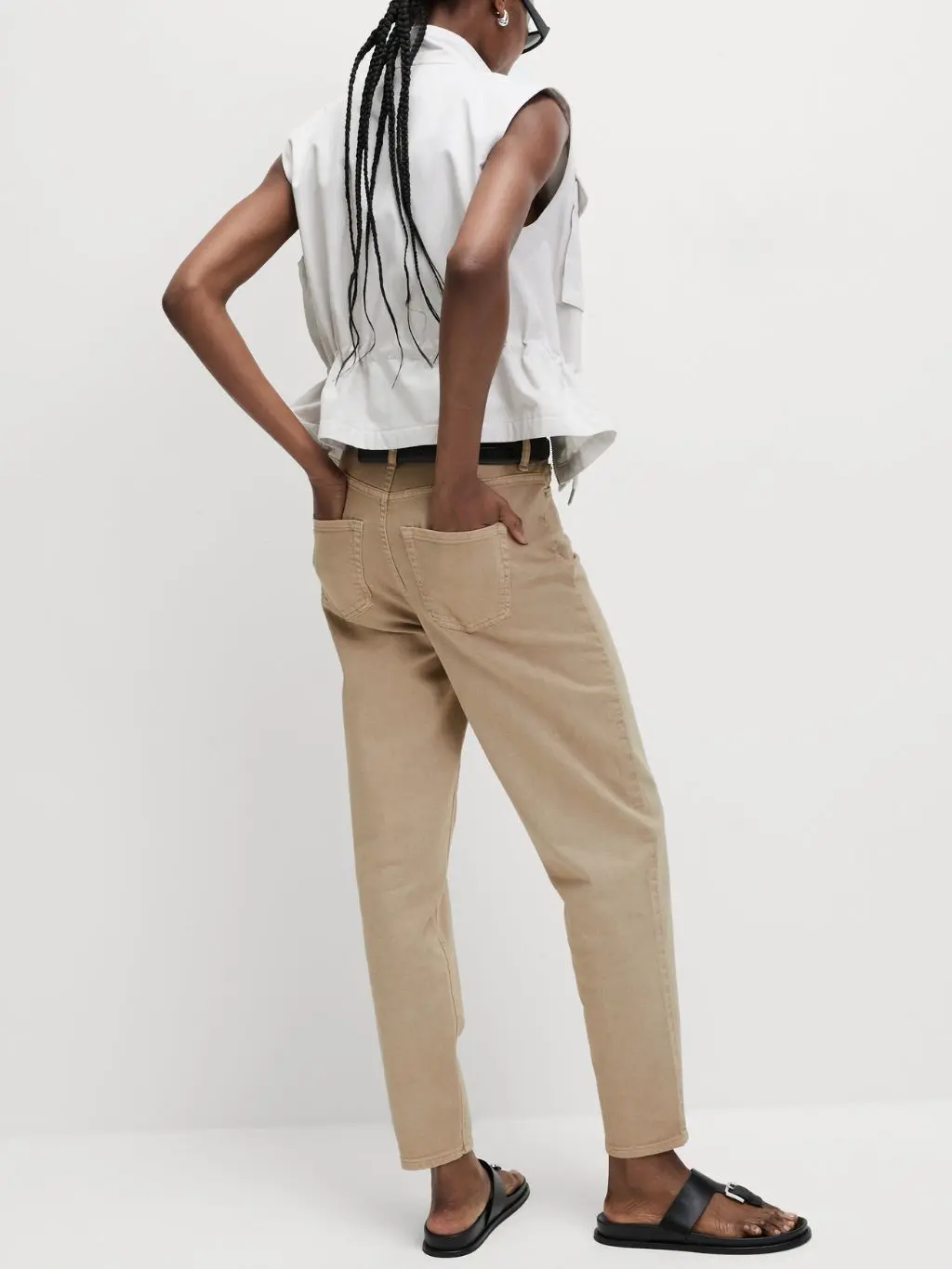 Woman wearing beige loose fit summer jeans, black sandals and white sleeveless jacket