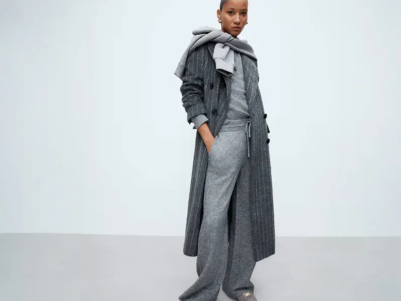 Woman wearing matching grey sweater set with a long grey coat and sweatshirt over her shoulders