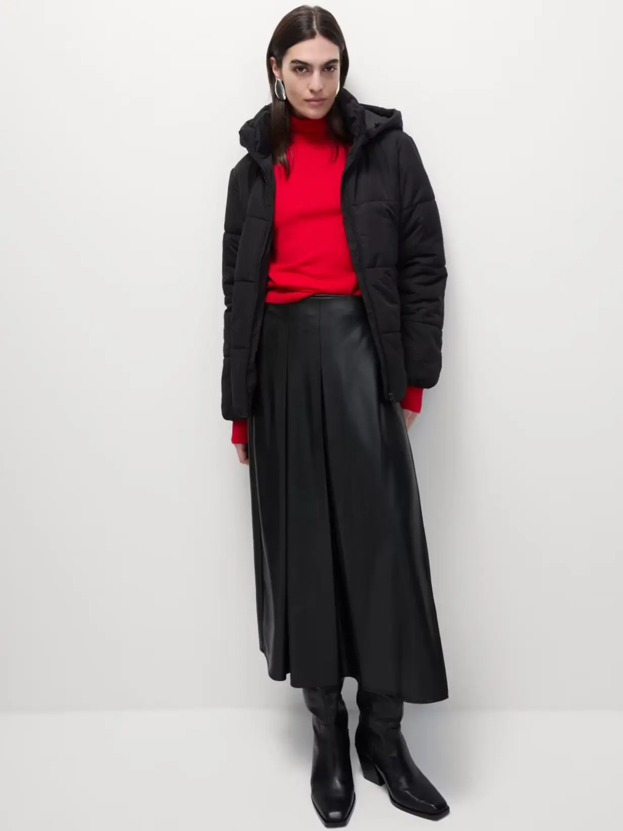 A woman wearing a red jumper, leather skirt and black puffer jacket