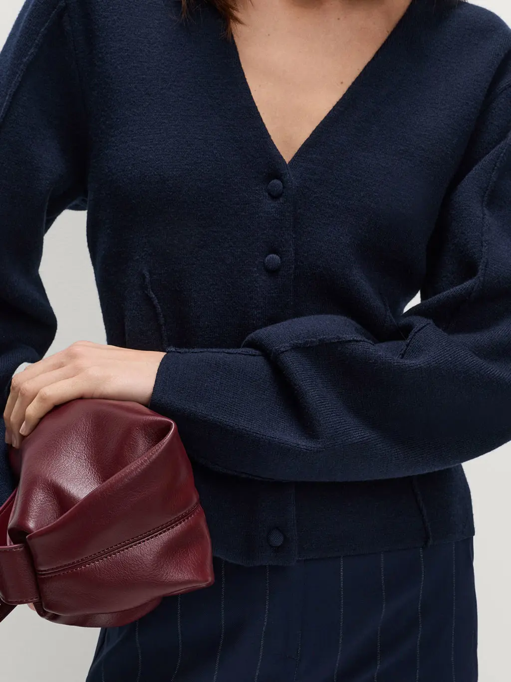 Woman wearing a navy cardigan with pinstriped trousers and a burgundy cross-body bag