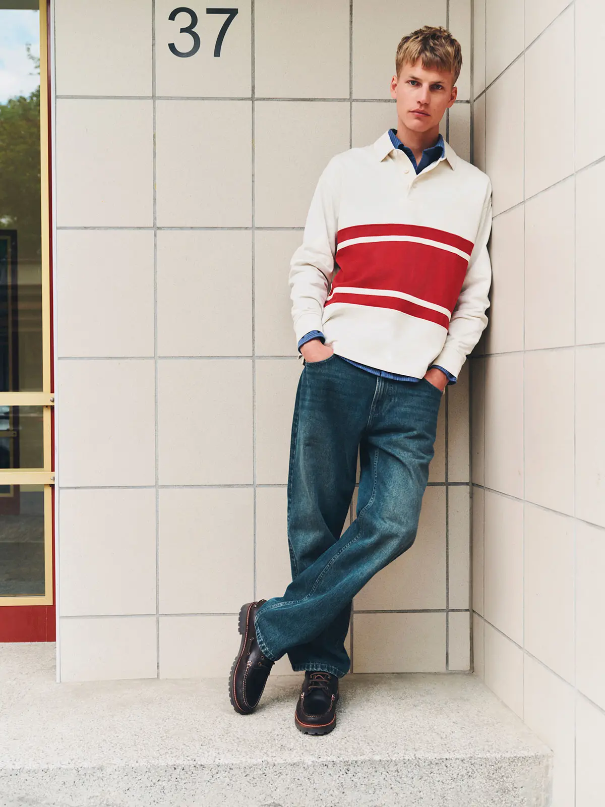 Man wearing red and white polo top, blue jeans and brown shoes 