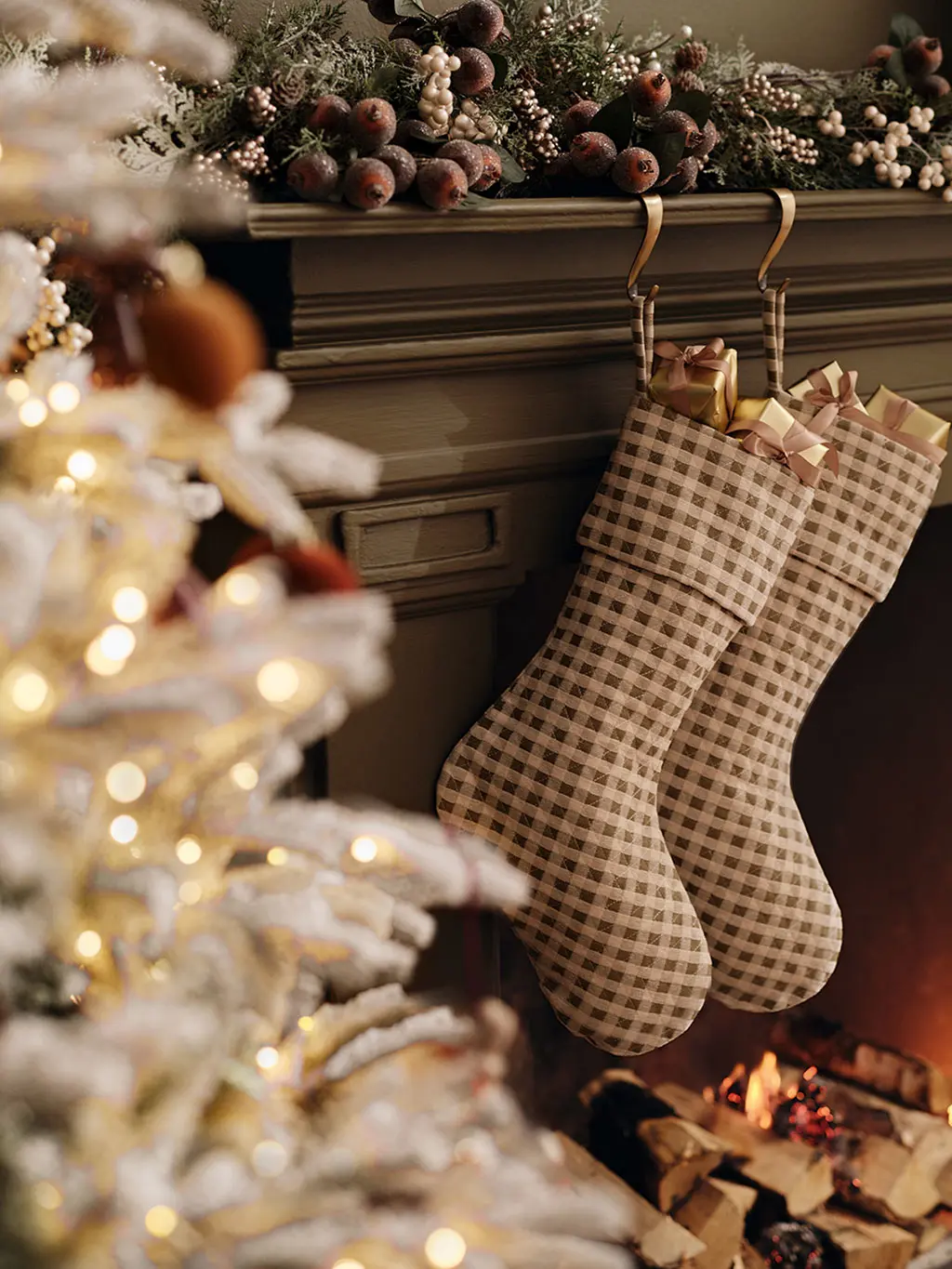 Christmas stockings hanging off a mantlepiece decorated with greenery, beside a Christmas tree
