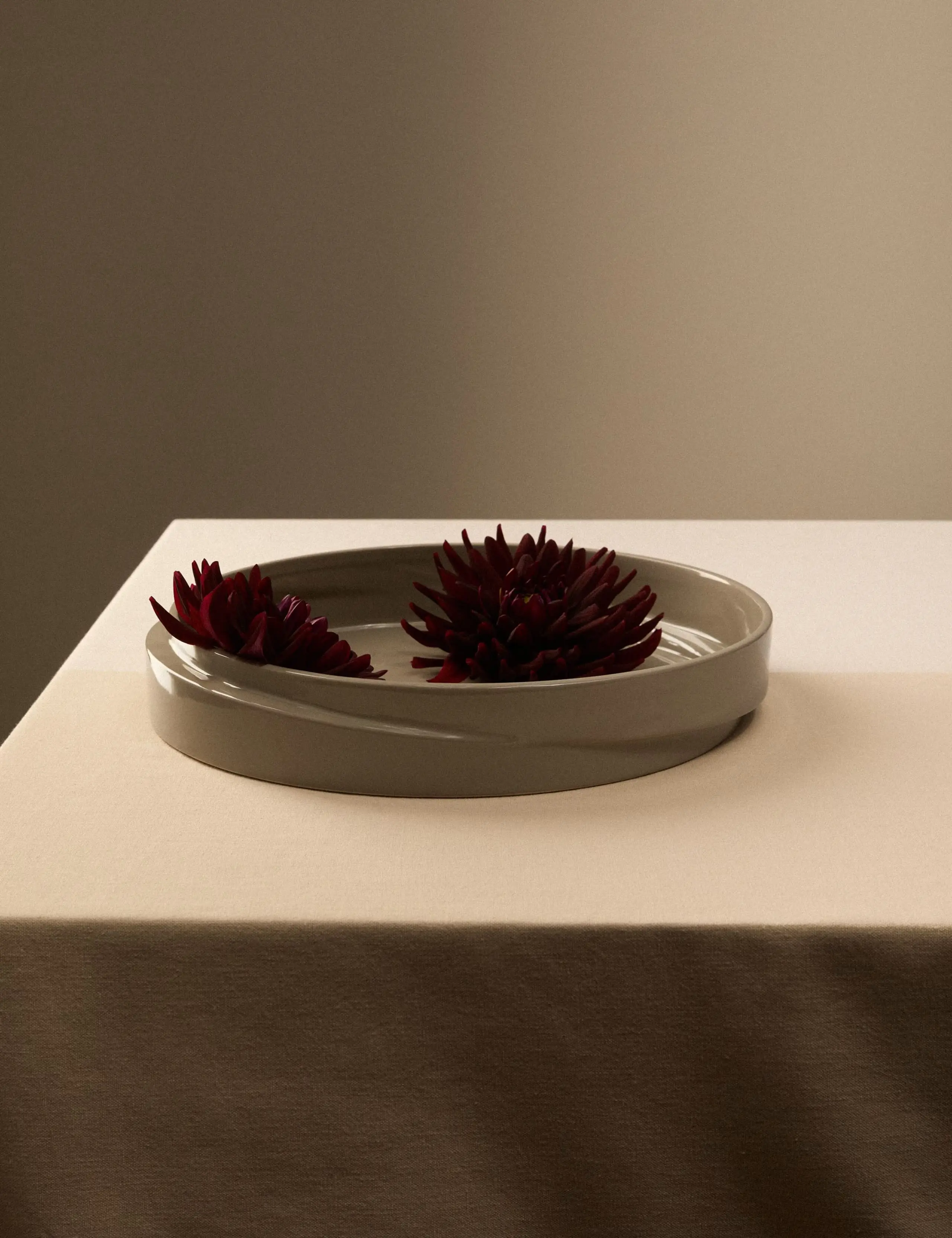 Beige ceramic bowl on a neutral table, filled with red flowers.