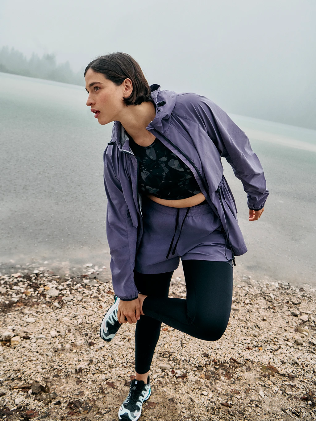 Woman wearing purple waterproof sports jacket, black sports bra, purple shorts and black leggings