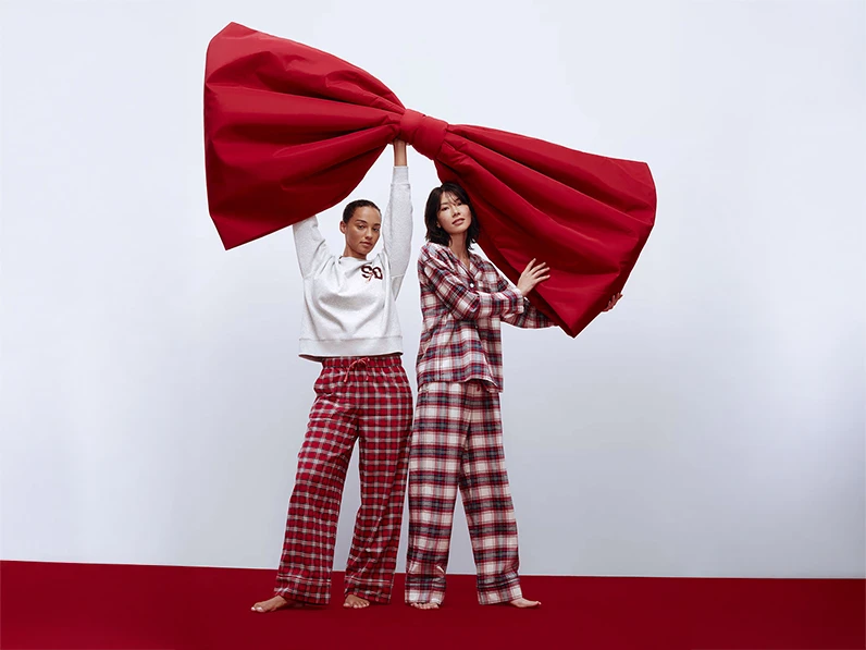 Two women wearing Christmas pyjamas holding a giant bow