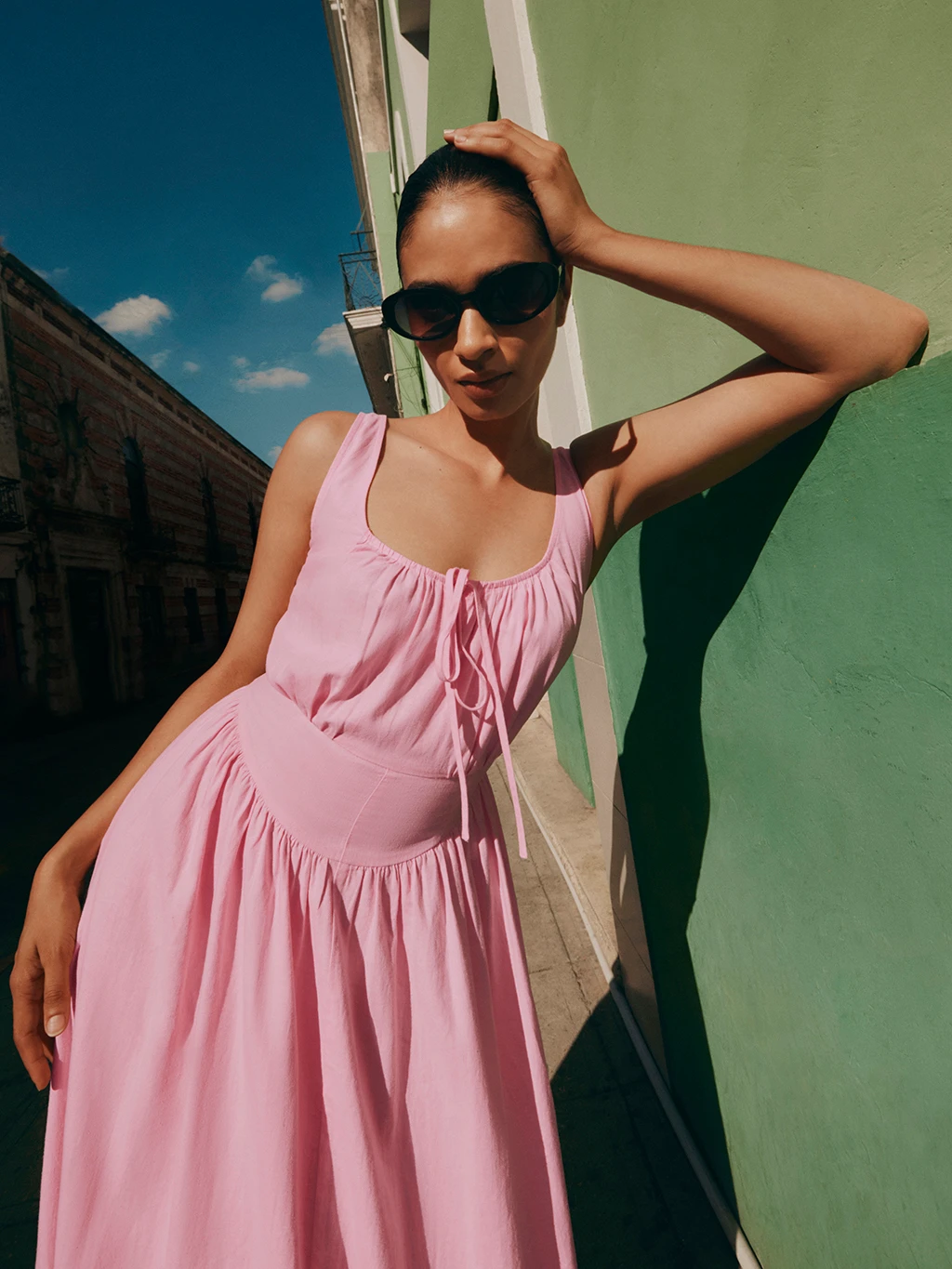 A woman wears a pink linen-rich dress with black sunglasses