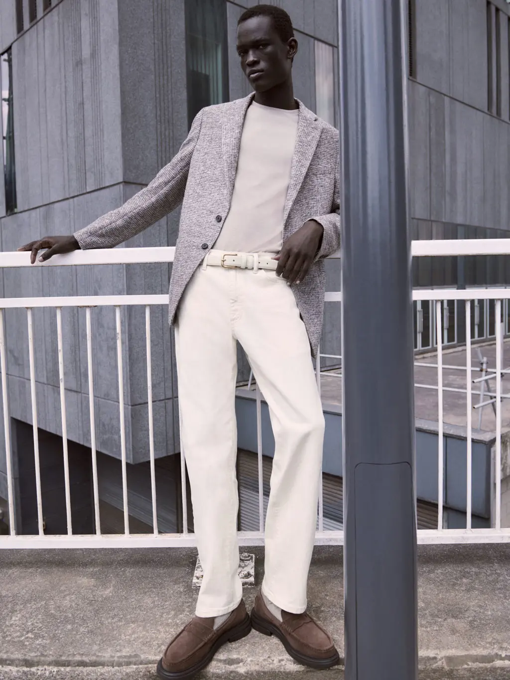 Man wearing white jeans, a beige T-shirt and grey blazer