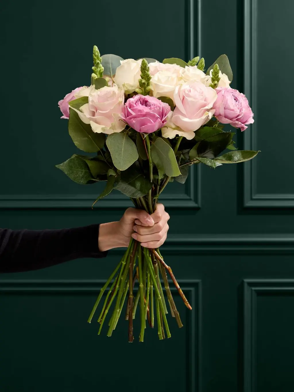 A hand holds a bouquet of roses and eucalyptus