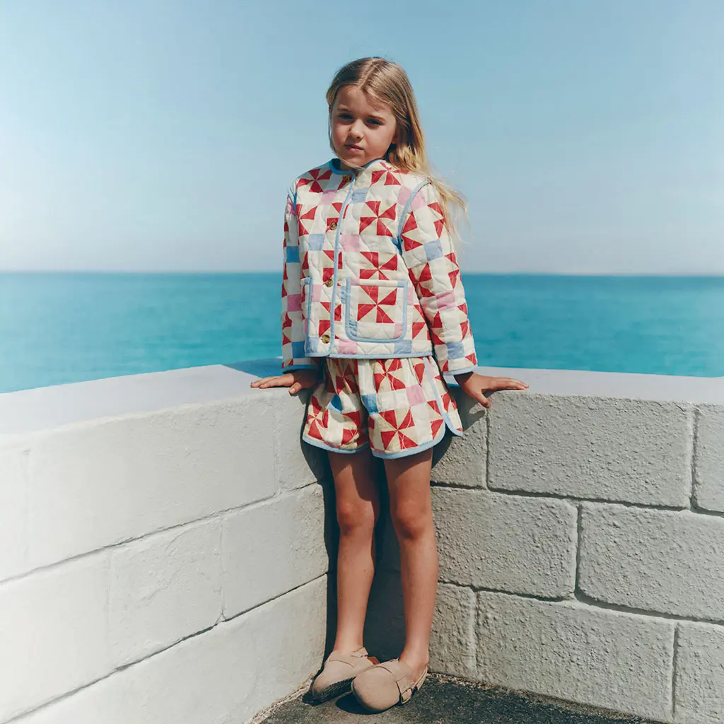Girl wearing matching quilted jacket and shorts with slip-on sandals