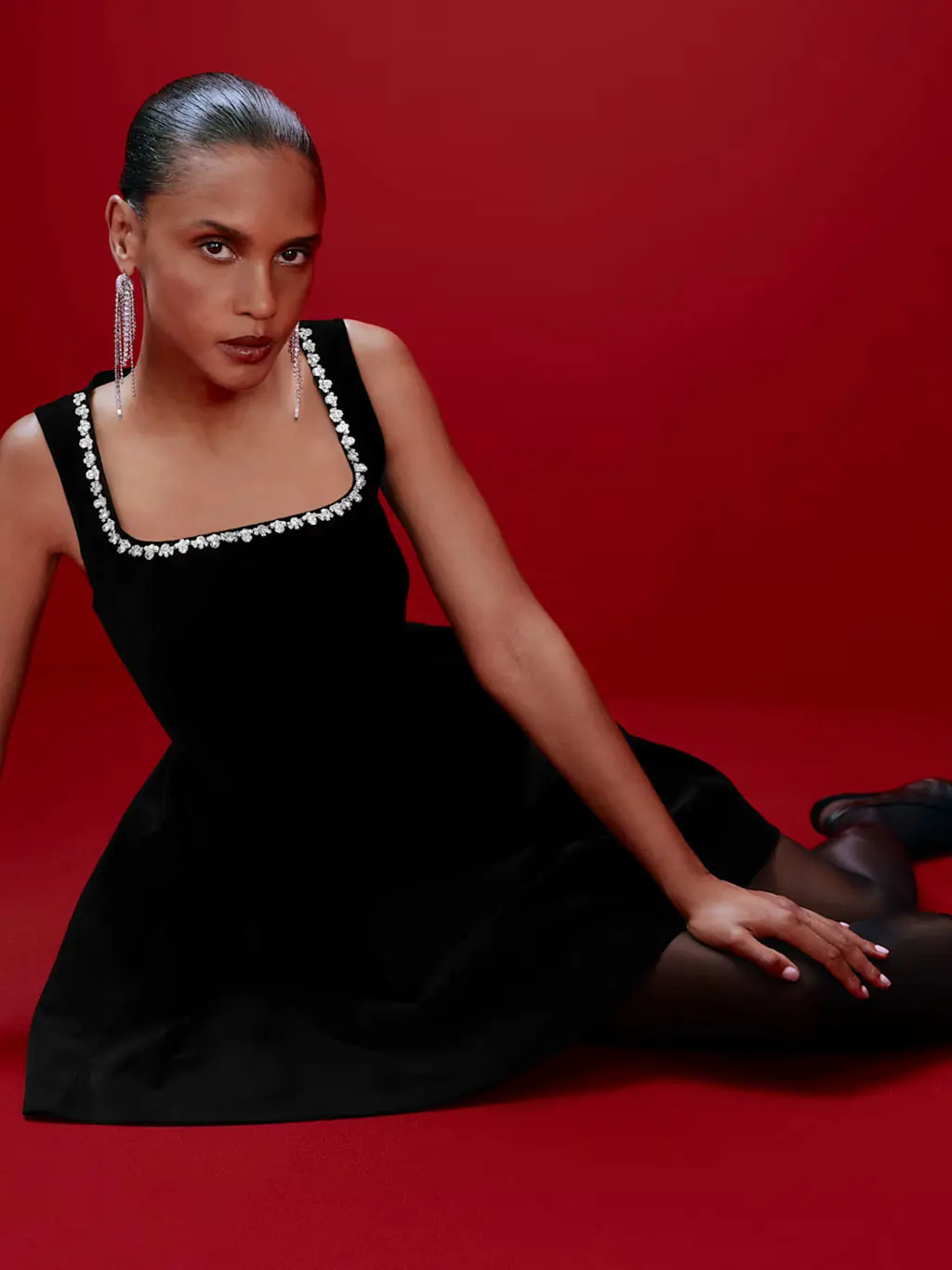 Woman in black embellished dress with silver drop earrings, black tights and heels