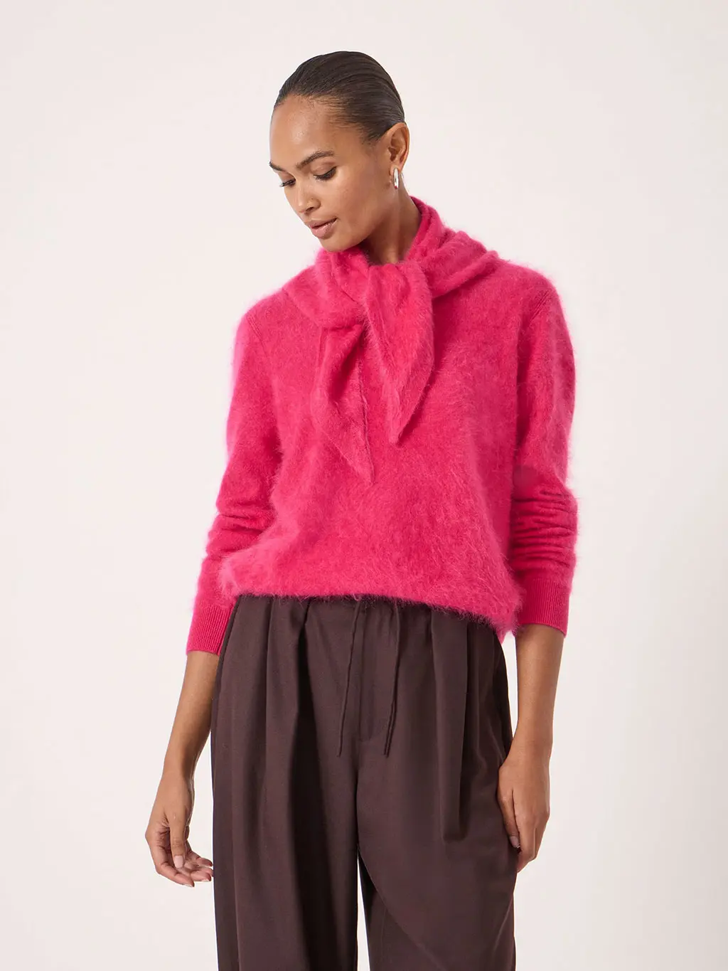 Woman wearing a pink cashmere scarf with a matching jumper and brown trousers