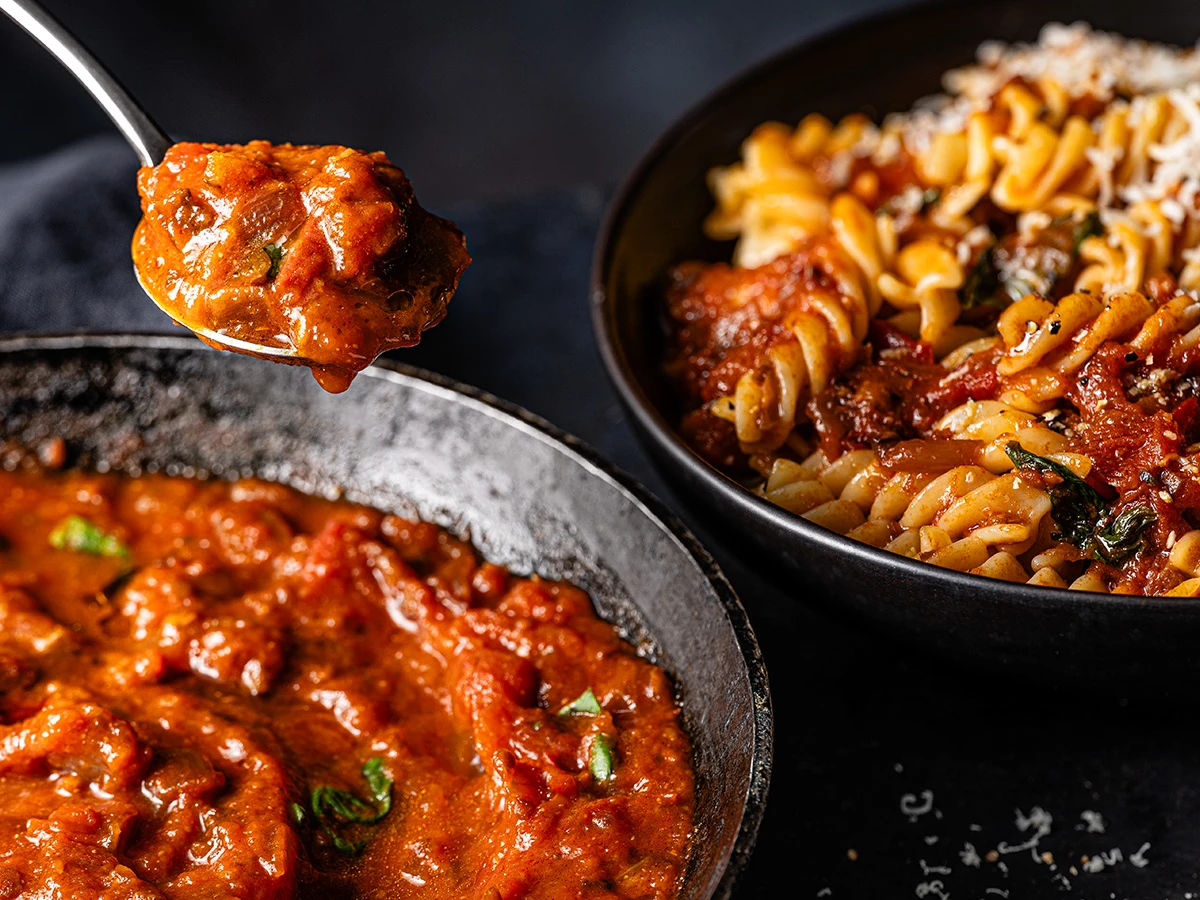 A pan of fresh tomato sauce with a bowl of pasta