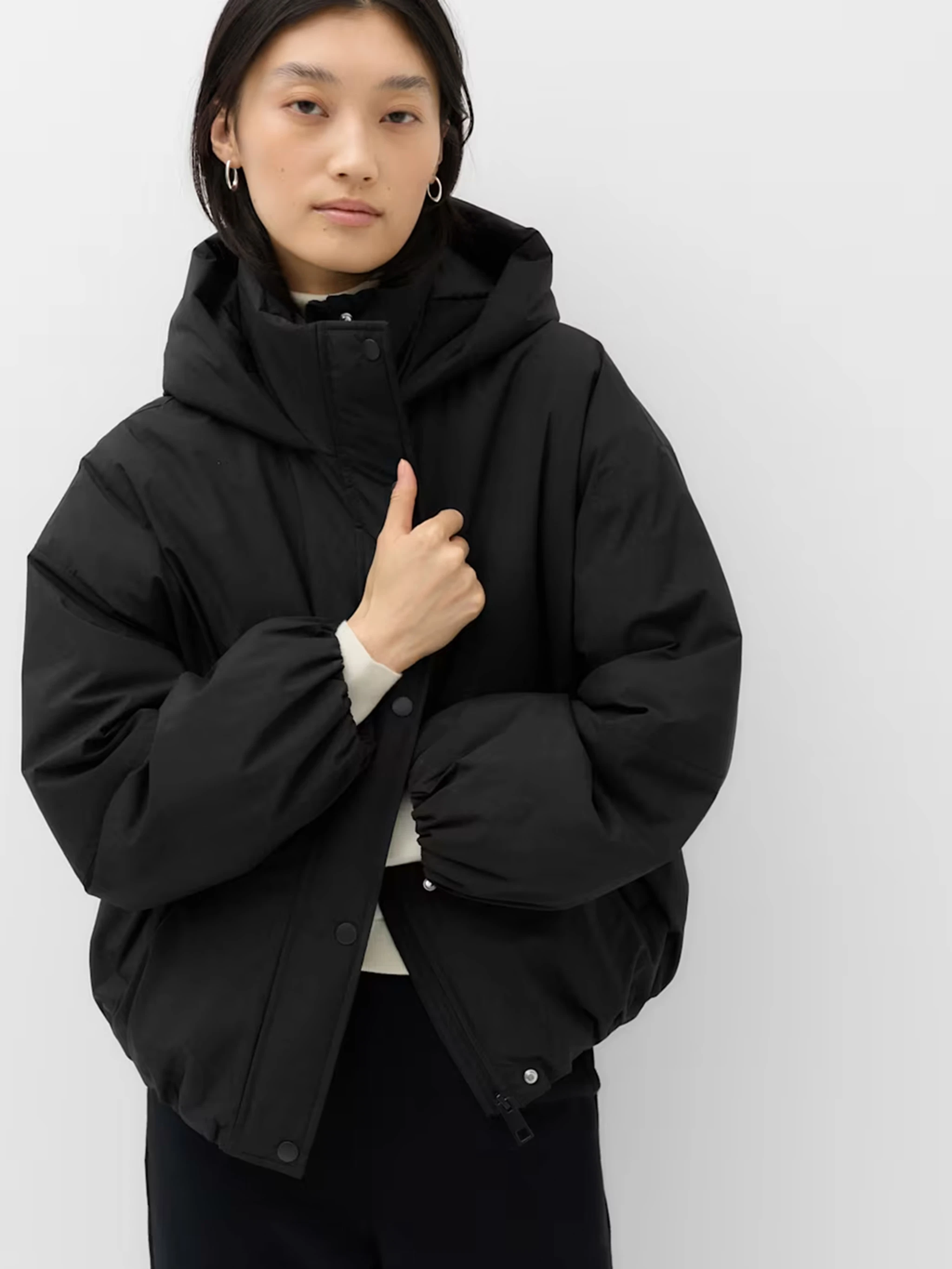Model wearing a black puffer coat with a hood and high neckline.