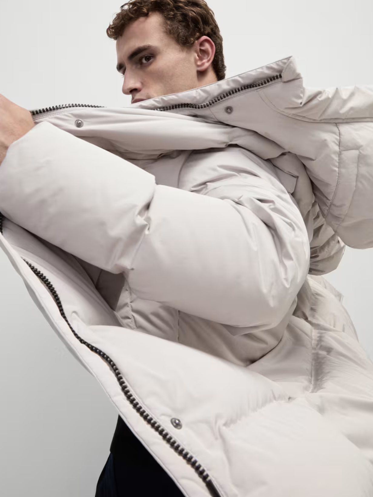 A man wearing a cream puffer coat stood against a light background