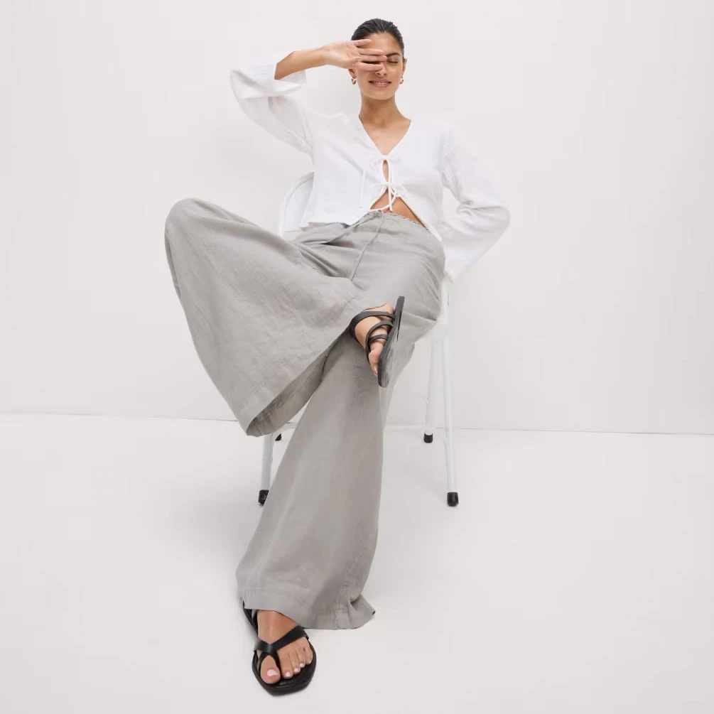 Woman wearing grey linen trousers with a white blouse and sandals