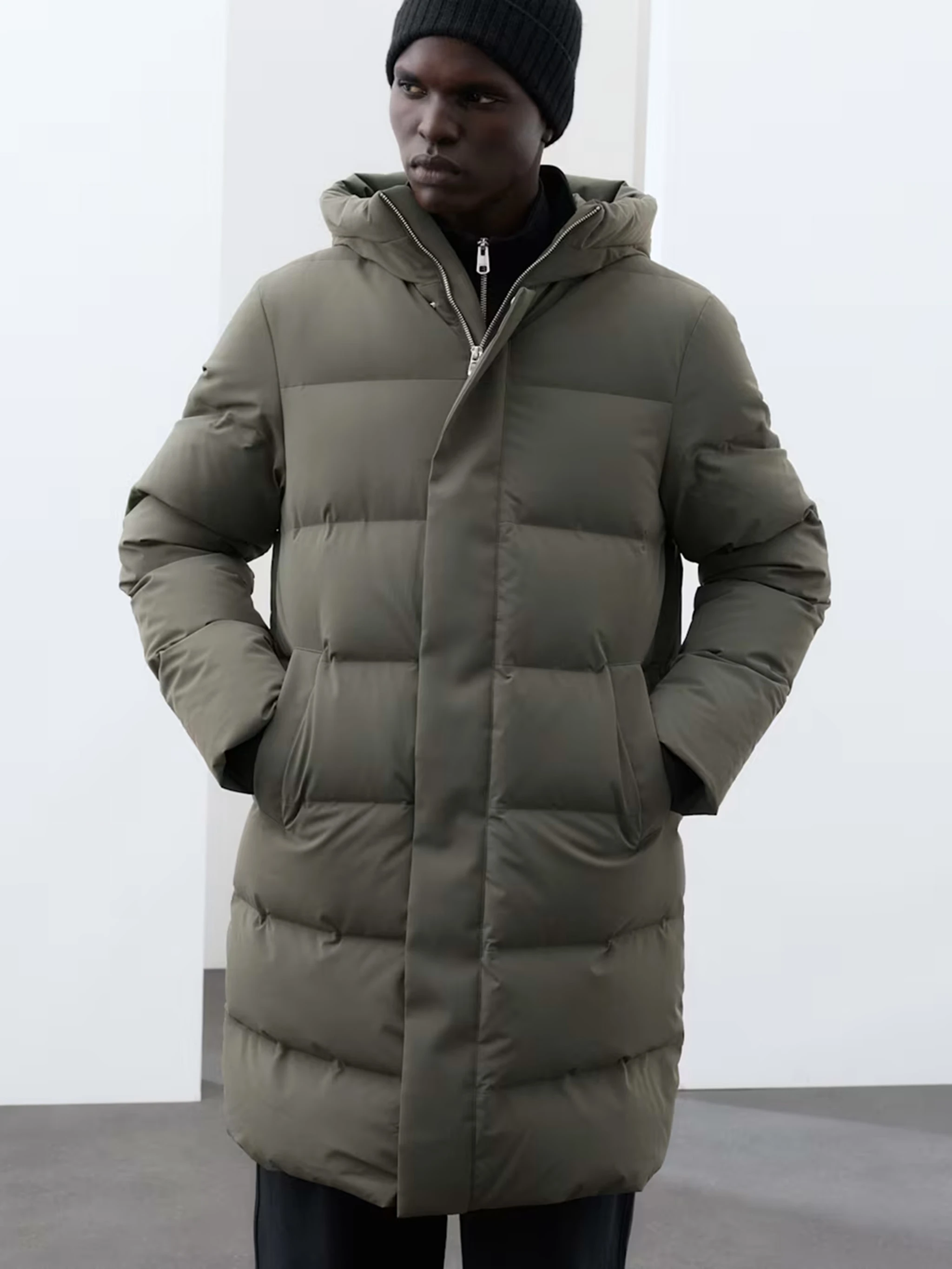 Man wearing a longline olive green puffer coat and a black beanie hat.