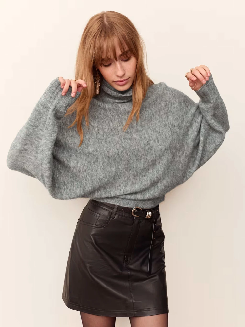 Model wearing a grey balloon sleeve jumper with a high roll neck, leather mini skirt and tights.