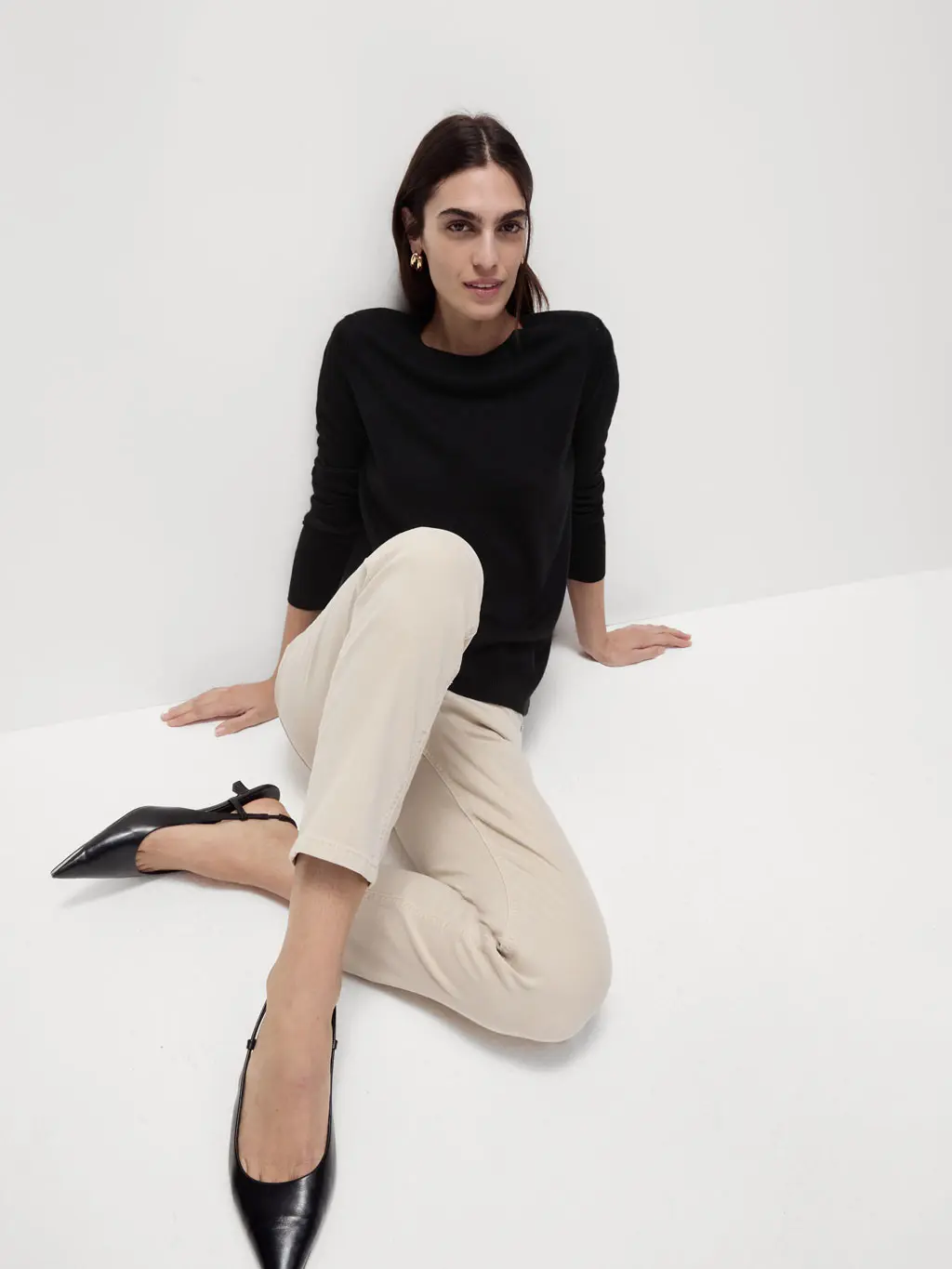 Woman wearing a black jumper with cream trousers and black kitten heels.