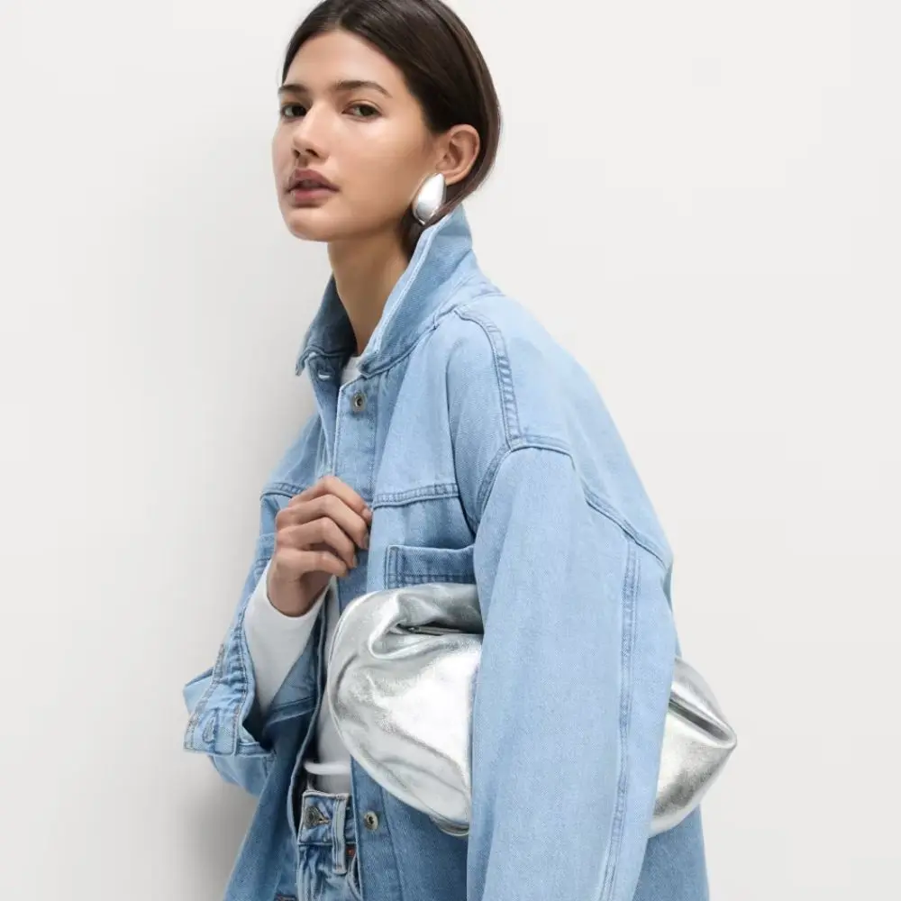 A model wearing a pale denim jacket with a large silver clutch bag under her arm