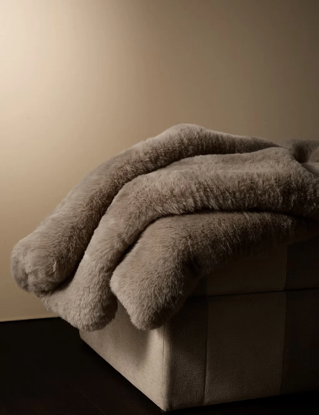 Taupe fluffy blanket folded on a fabric stool.