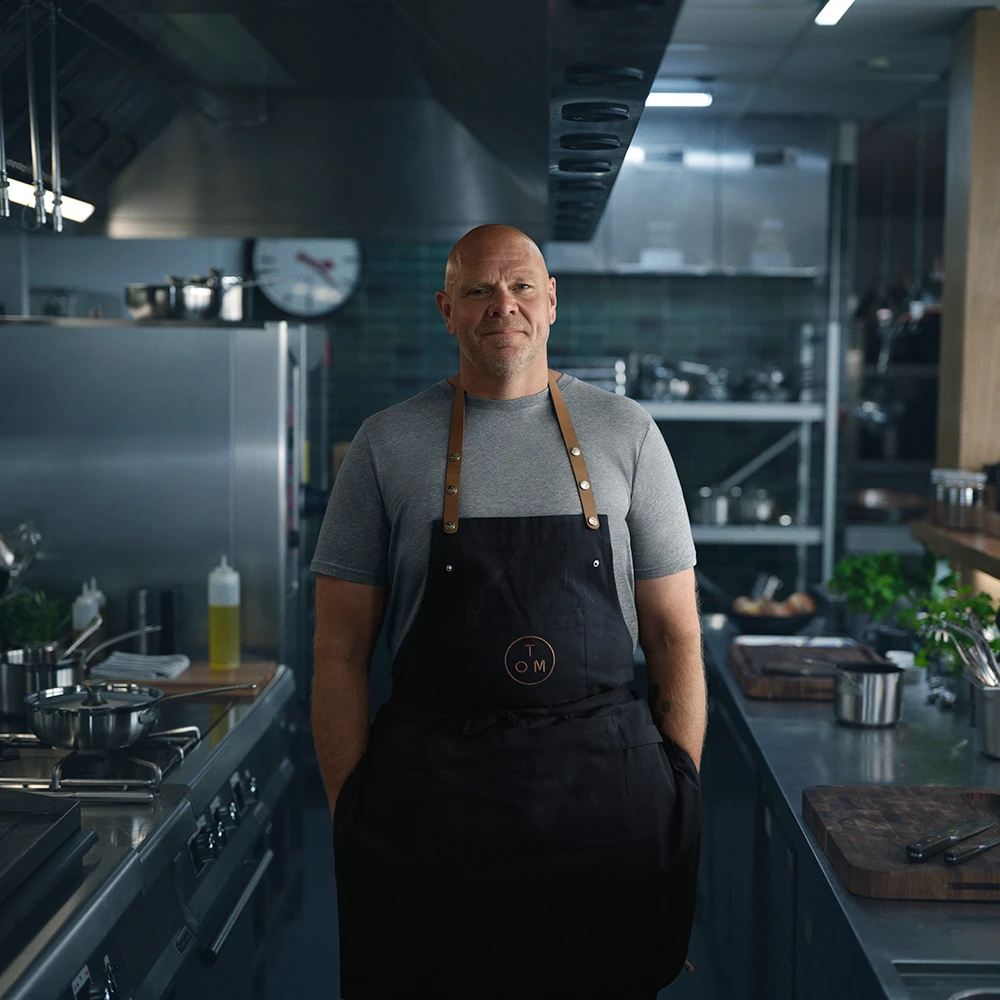 Tom Kerridge wearing a grey T-shirt and apron in a kitchen