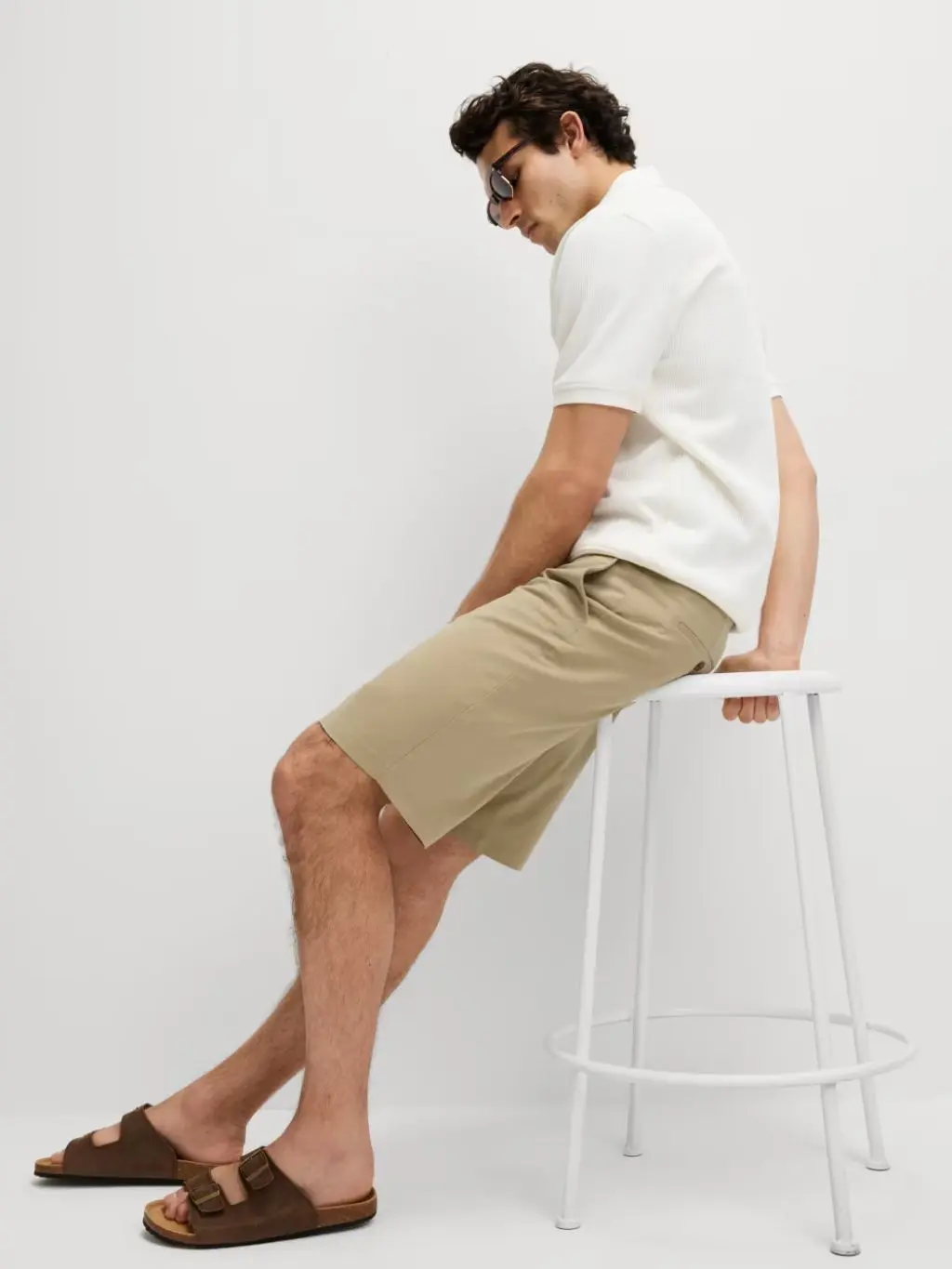 A man sat on a stool wearing smart longer length chino shorts and a polo shirt