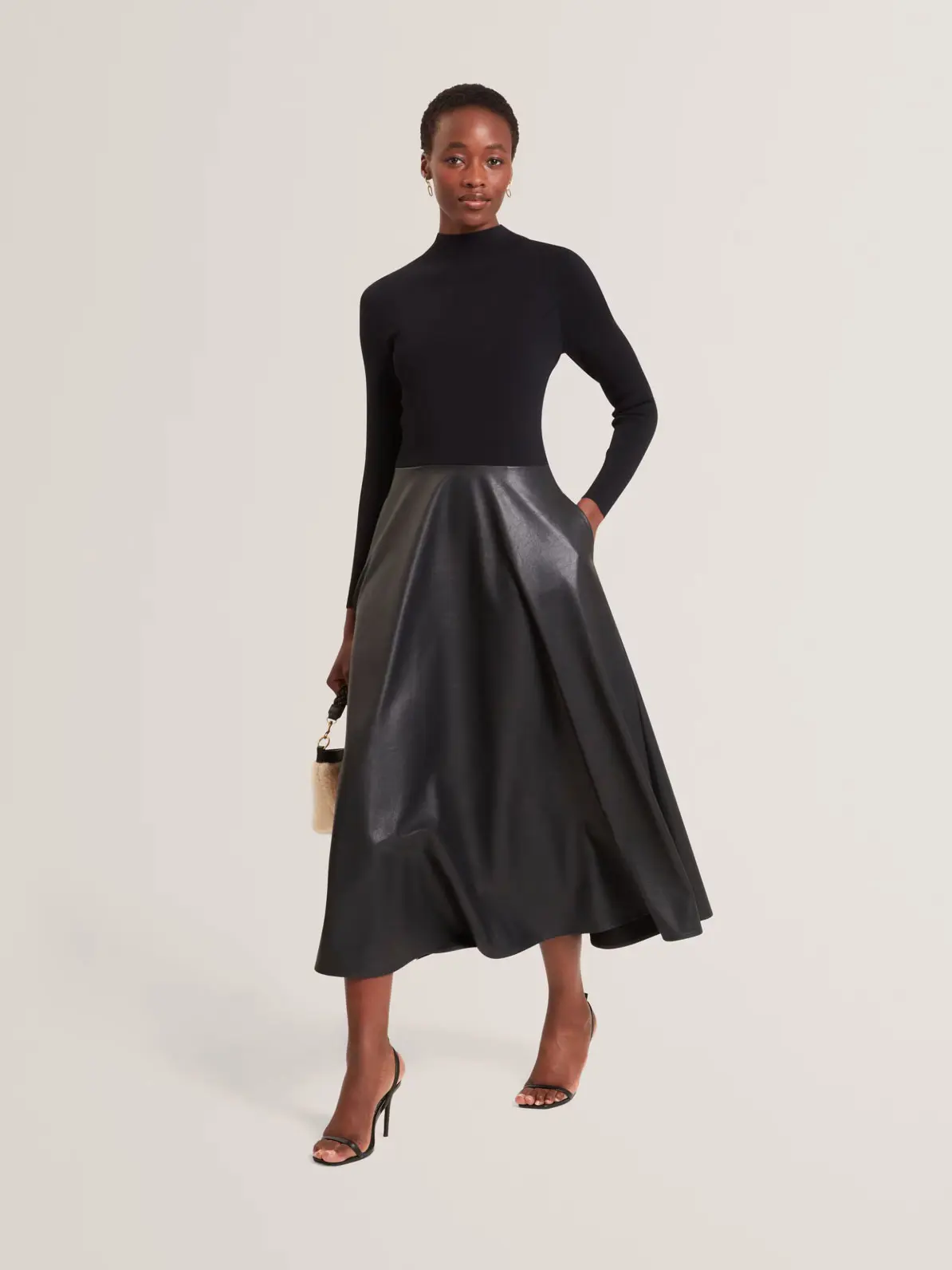Woman wearing long-sleeved black dress with a contrasting leather skirt