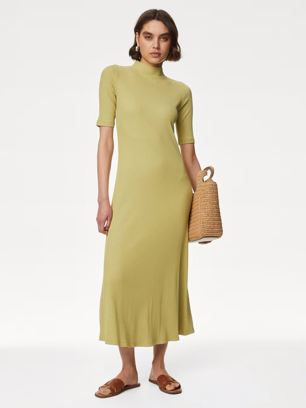 Woman wearing green dress and brown sandals, holding a straw bag