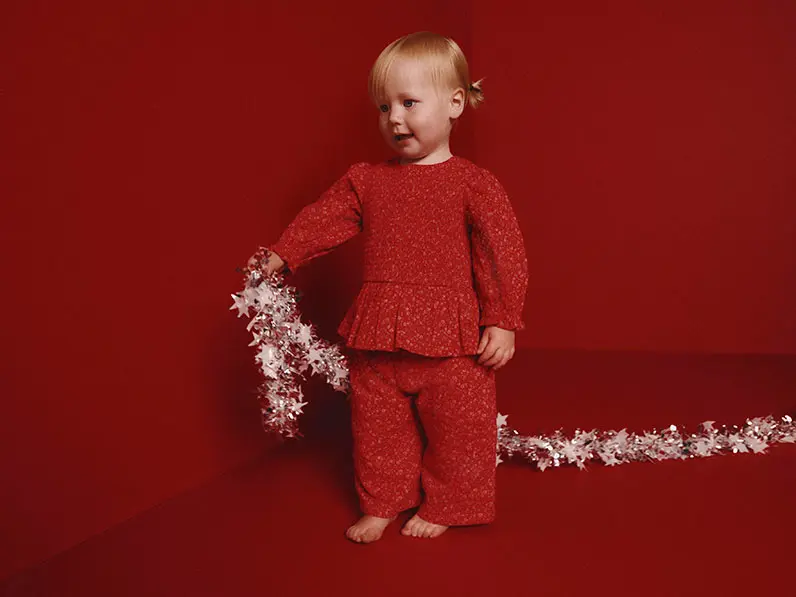 Young girl in a matching set of red pyjamas holding some tinsel.