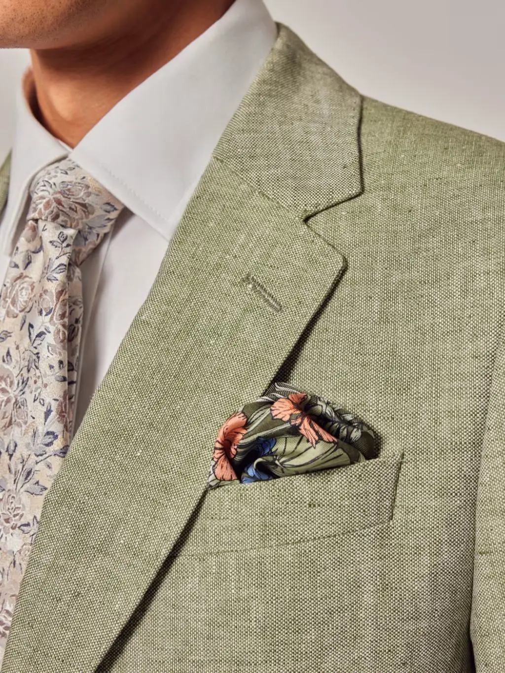A close up of a man wearing a floral tie, green suit and a floral pocket square