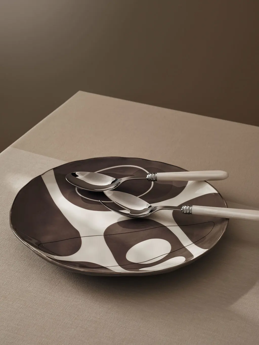 Brown and white ceramic serving bowl with a spot pattern, and two marble-effect spoons.