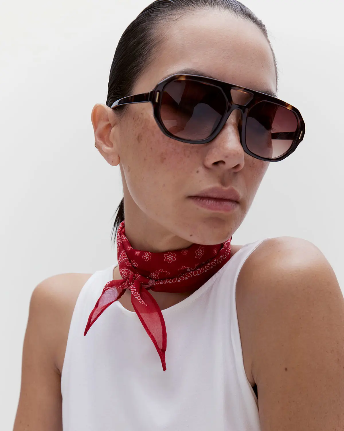 Woman wearing a white vest with a red bandana scarf and aviator sunglasses