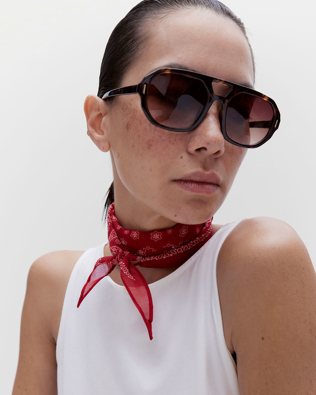 Woman wearing a white vest with a red bandana scarf and aviator sunglasses