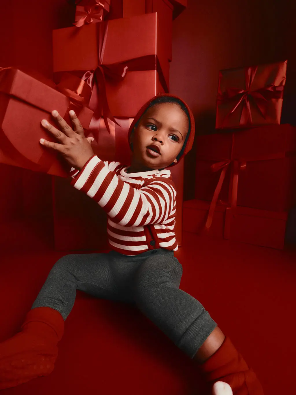 Young boy in a red and white striped t-shirt and grey leggings, surrounded by red presents.