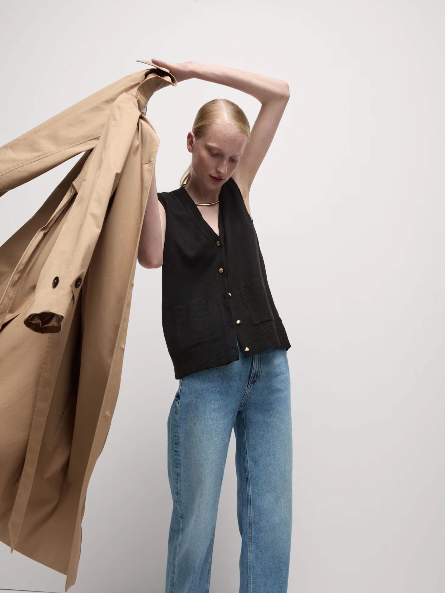 Woman wearing knitted waistcoat, jeans and trench coat