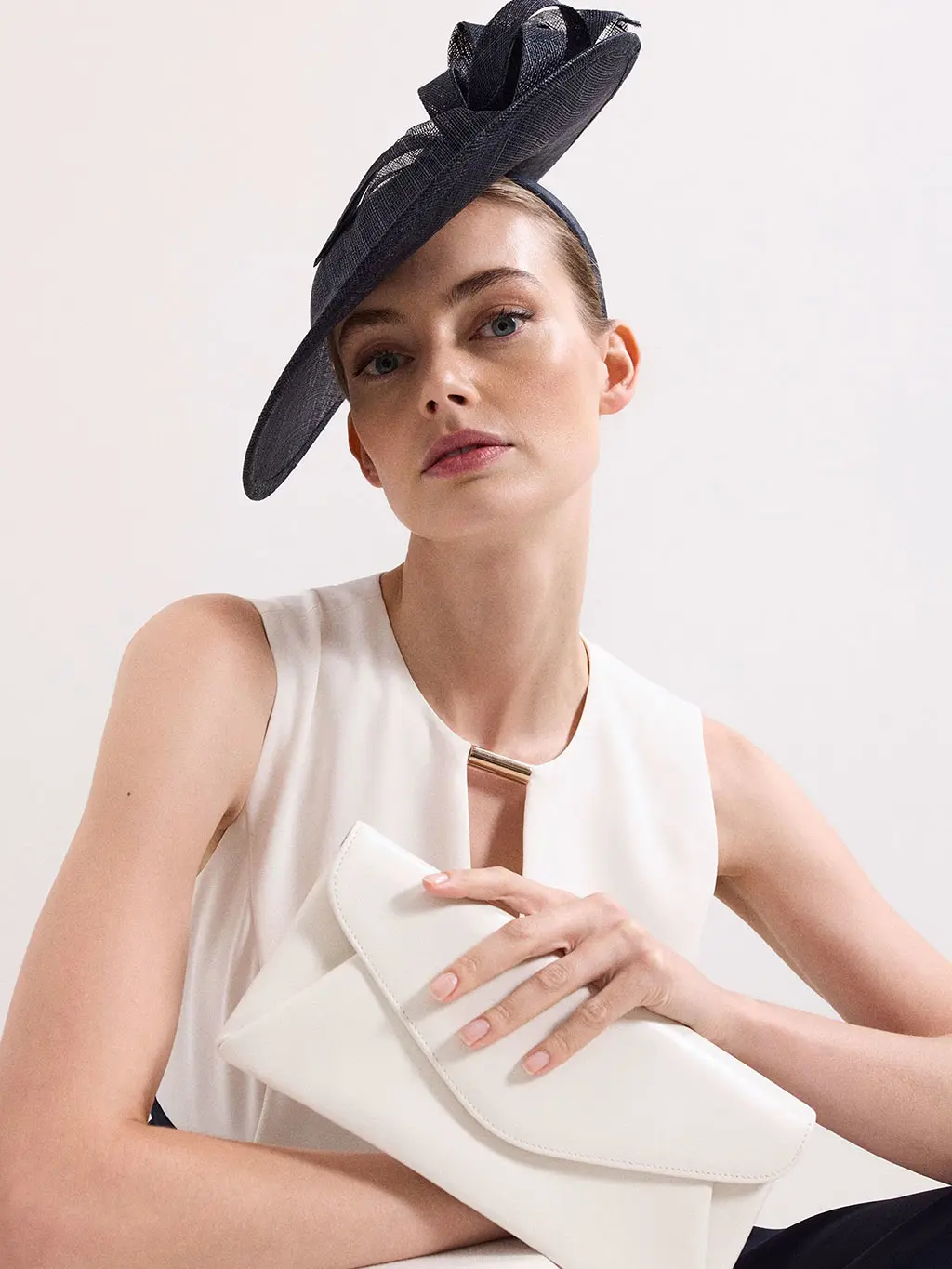 Woman wearing a navy fascinator with a white top and white clutch bag