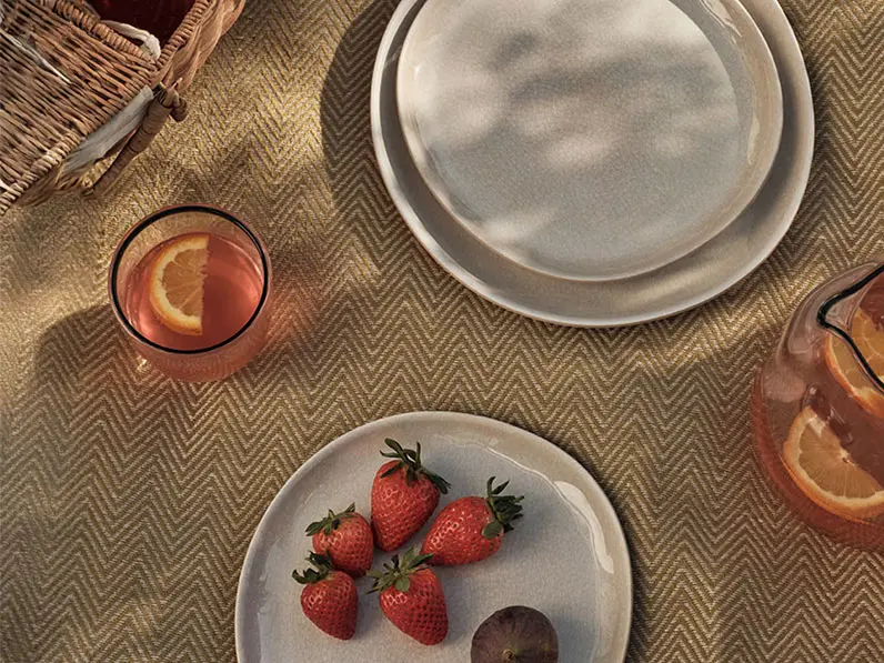 Picnic setup on a herringbone blanket with cream plates and a basket