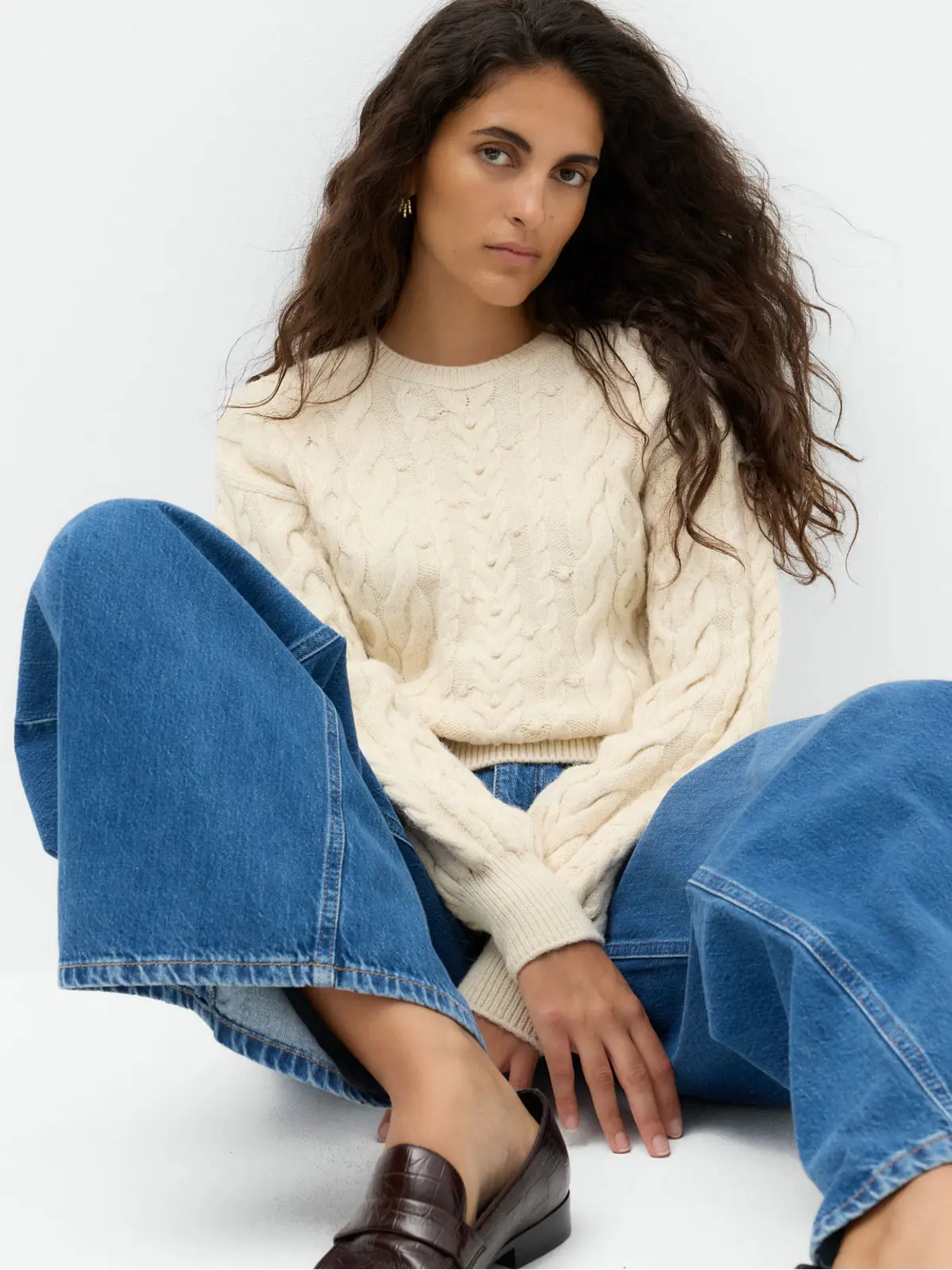 Woman wearing cream cable-knit jumper with blue jeans and loafers