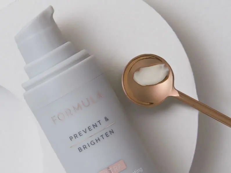 A close up of a Formula eye cream on a plate next to a copper spoon containing the cream