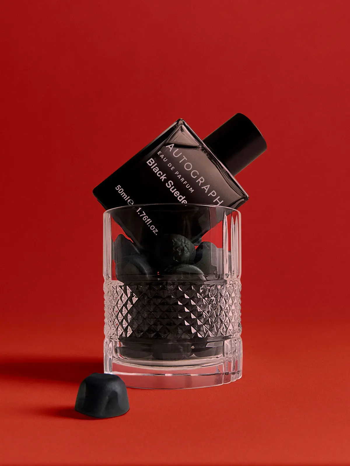 Glass holding men's Autograph fragrance in black bottle 